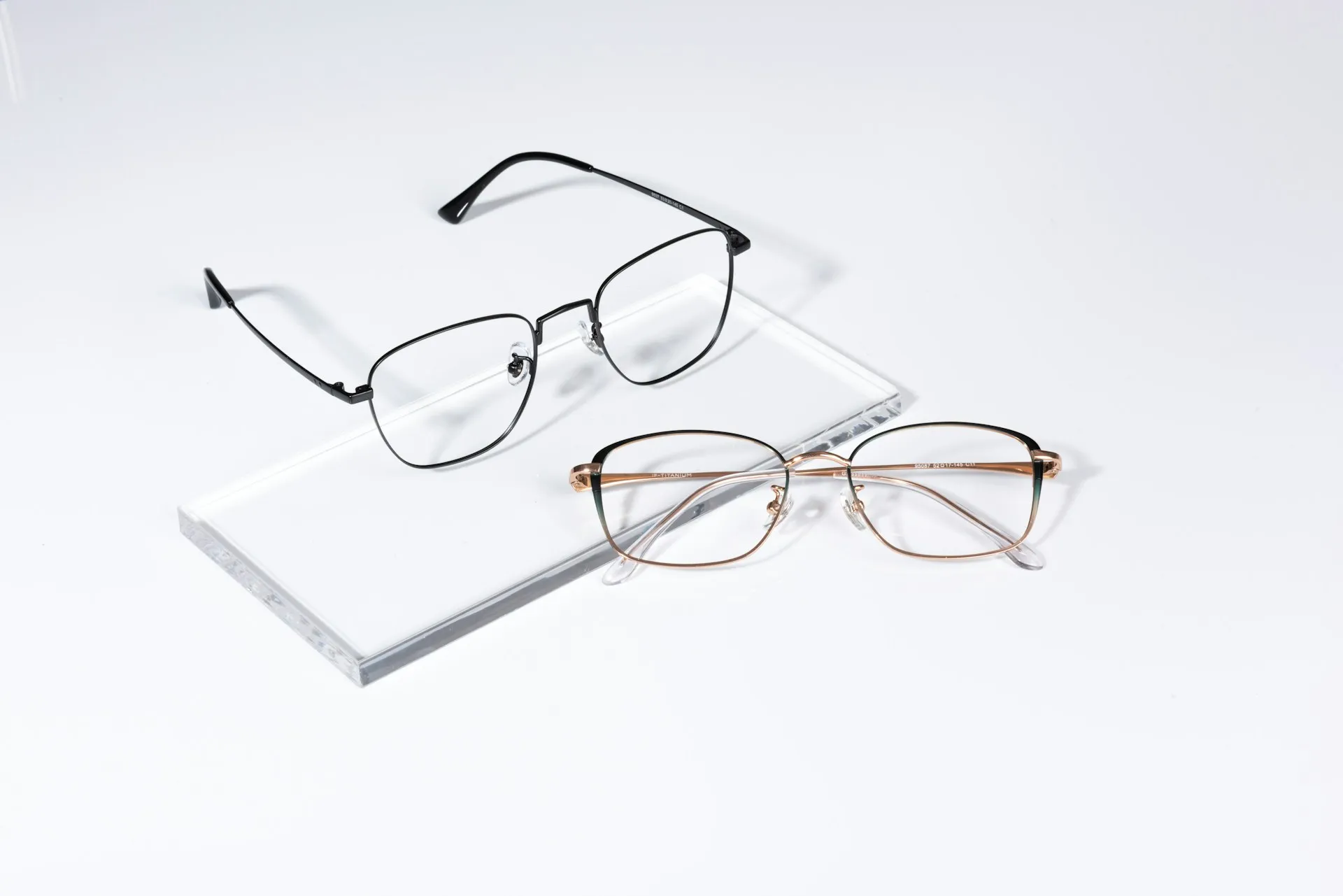 Дві металеві оправи — чорна та золотиста — на білому тлі